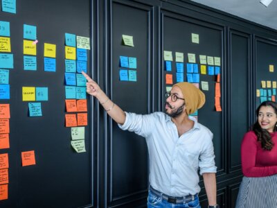 Σχεδιαστής εξηγεί ένα πλάνο με χαρτάκια σε μαύρο τοίχο